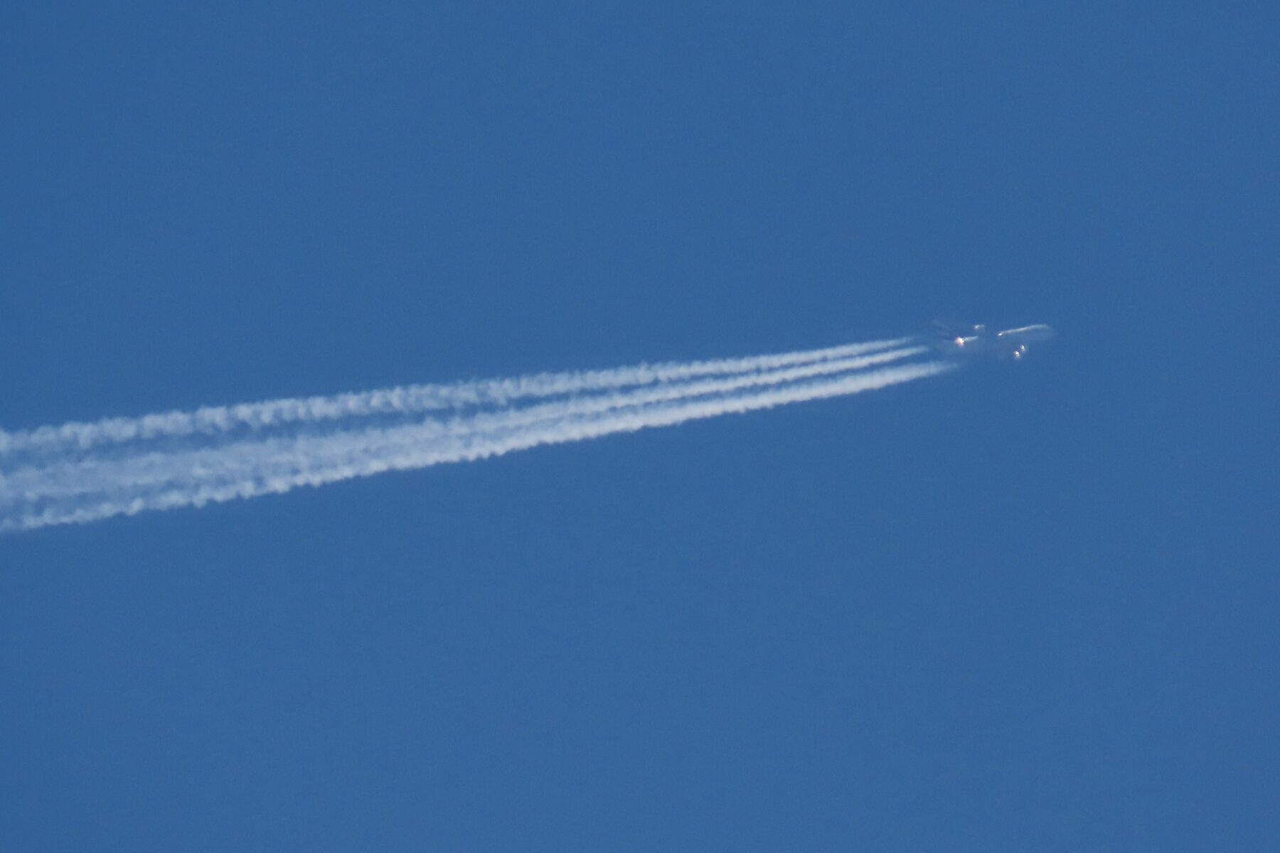 A cruising airliner at high altitude trailing four white condensation trails across a clear blue sky