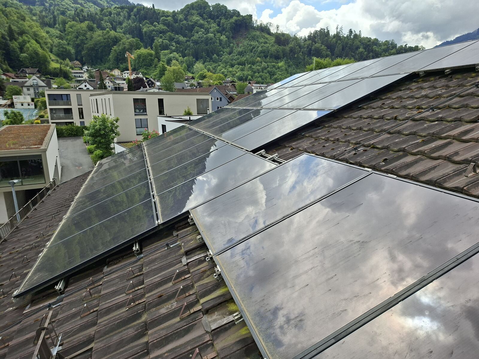 Rooftop photovoltaic modules on a tiled roof, their glass dulled and streaked with pollen and dust, in an alpine valley town